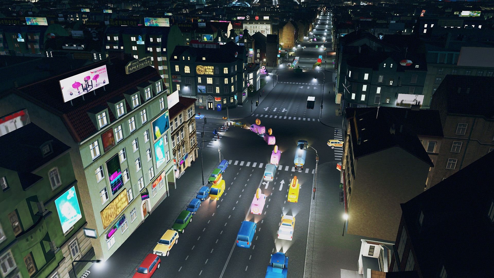 A night-time view of a busy intersection in a city, with a line of vehicles nearby and a couple of lavender vans turning left.