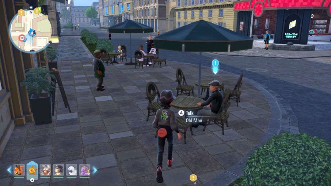 Outside the cafe, an old man sits at a table with a large umbrella over it.